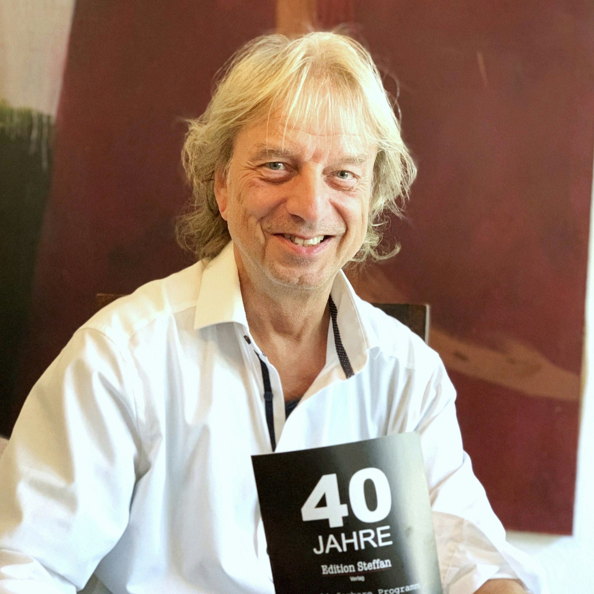 Frank Steffan hält ein Prospekt zu seinem Firmenjubiläum in den Händen.