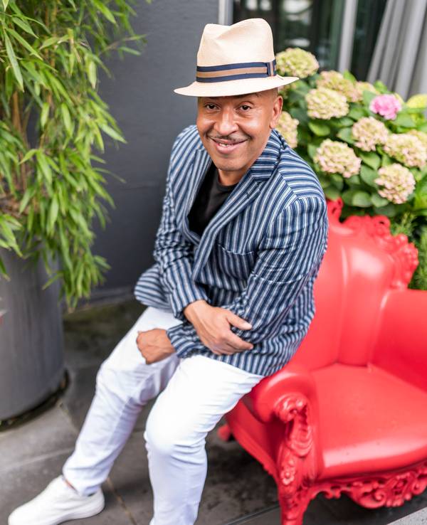 Lou Bega sitzt auf einem roten Sessel und lächelt in die Kamera.