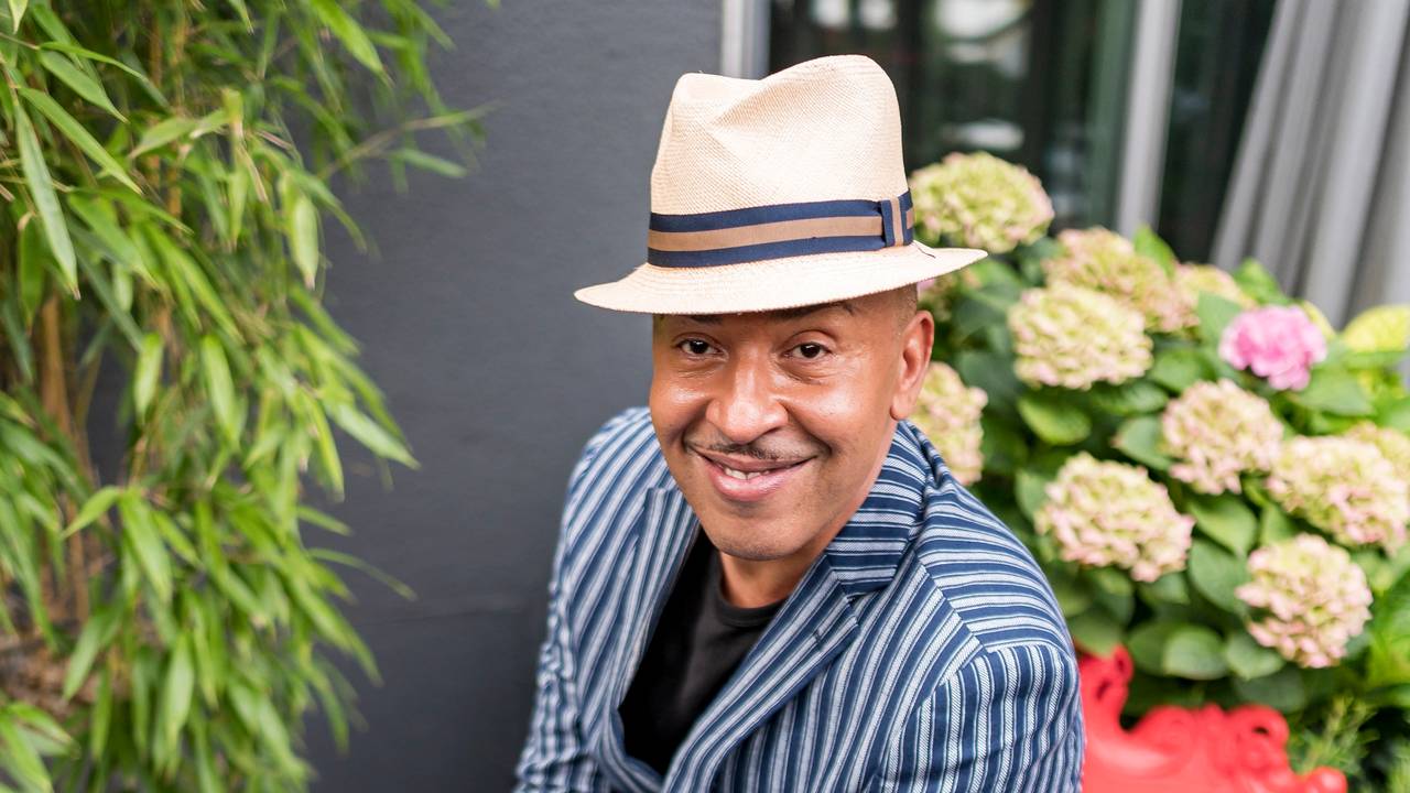Lou Bega sitzt auf einem roten Sessel und lächelt in die Kamera.