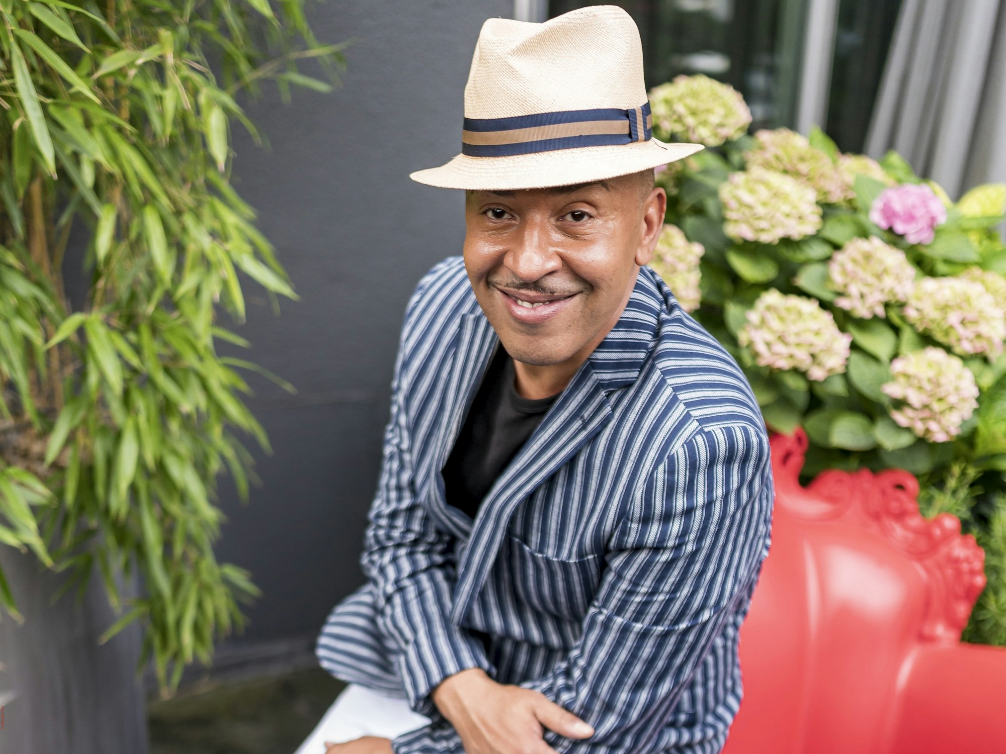 Lou Bega sitzt auf einem roten Sessel und lächelt in die Kamera.