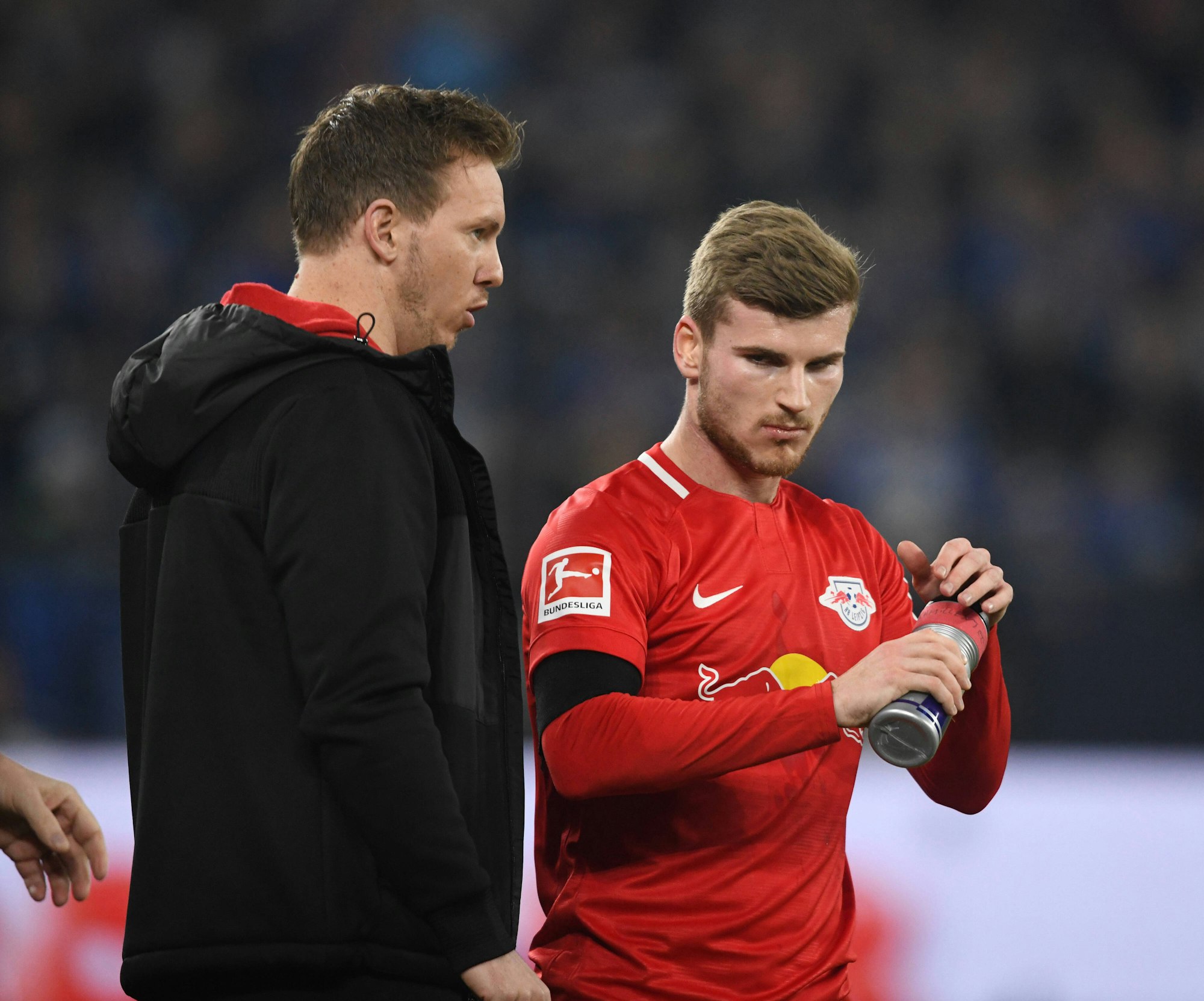Julian Nagelsmann spricht mit Timo Werner, welcher seine Trinkflasche in beiden Händen hält.