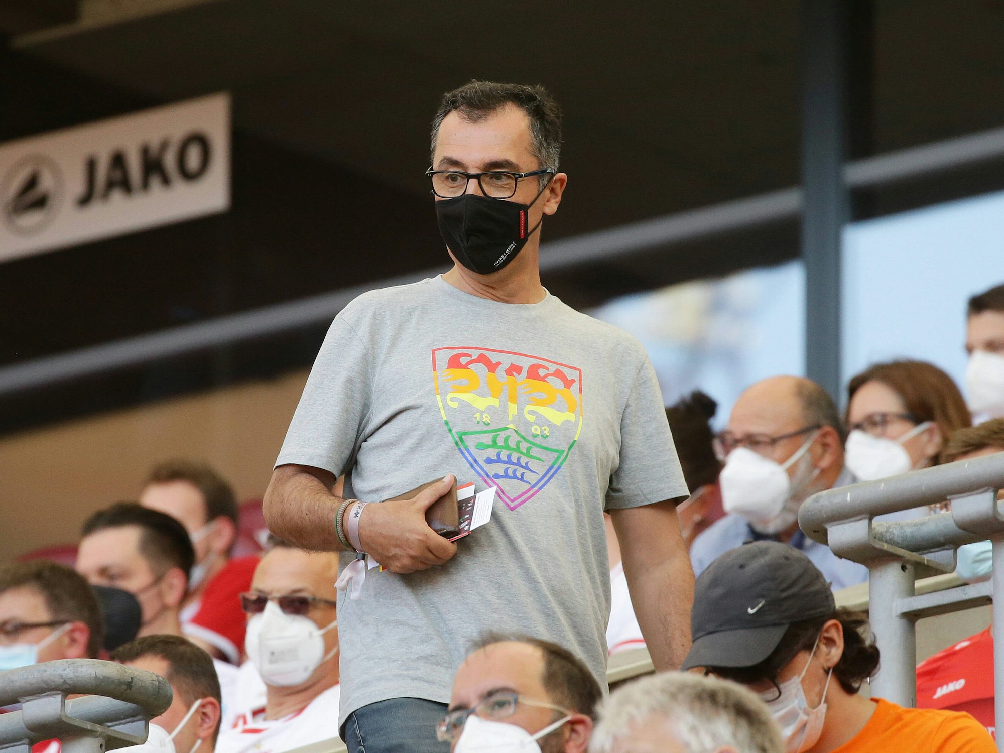 Cem Özdemir trägt ein graues Shirt mit einem bunten VfB-Wappen.