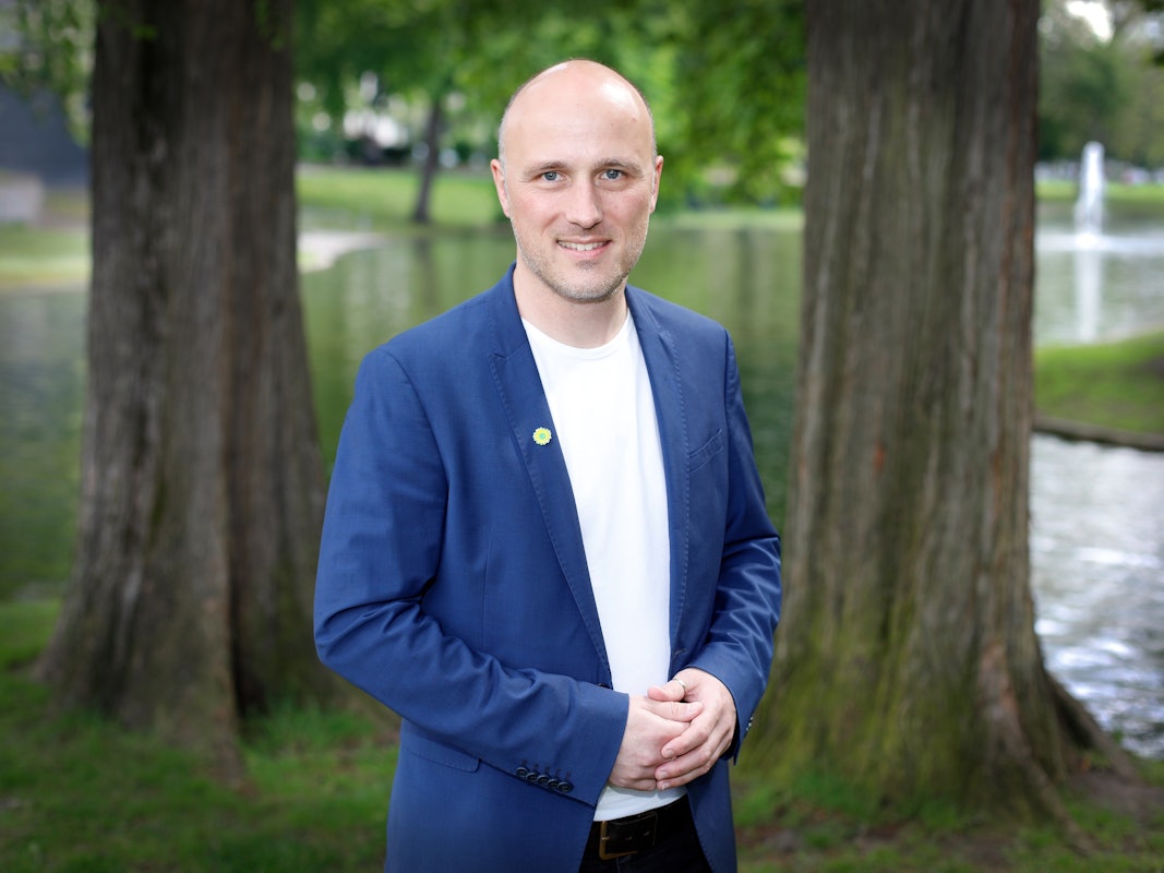 Sven Lehmann steht vor einem See mit Bäumen und lächelt in die Kamera.