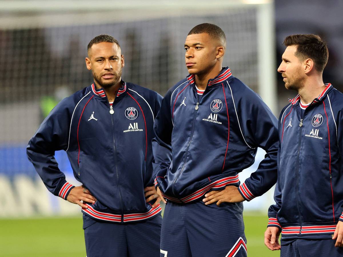 Neymar, Kylian Mbappe und Lionel Messi stehen in Trainingsjacken auf dem Feld. Neymar und Mbappe haben die Hände in den Hüften.