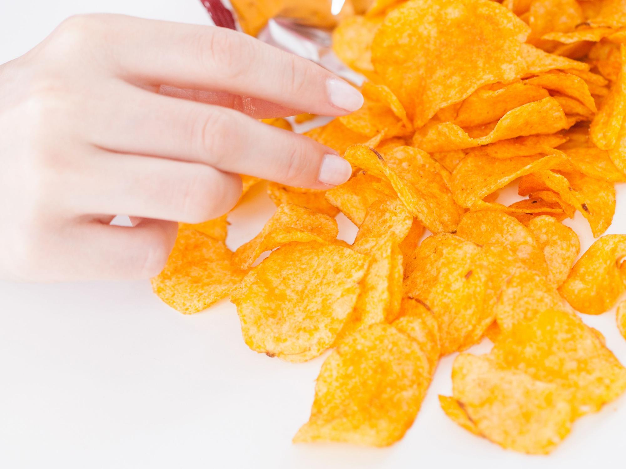 Das Symbolfoto zeigt eine Hand, die nach Kartoffelchips greift.