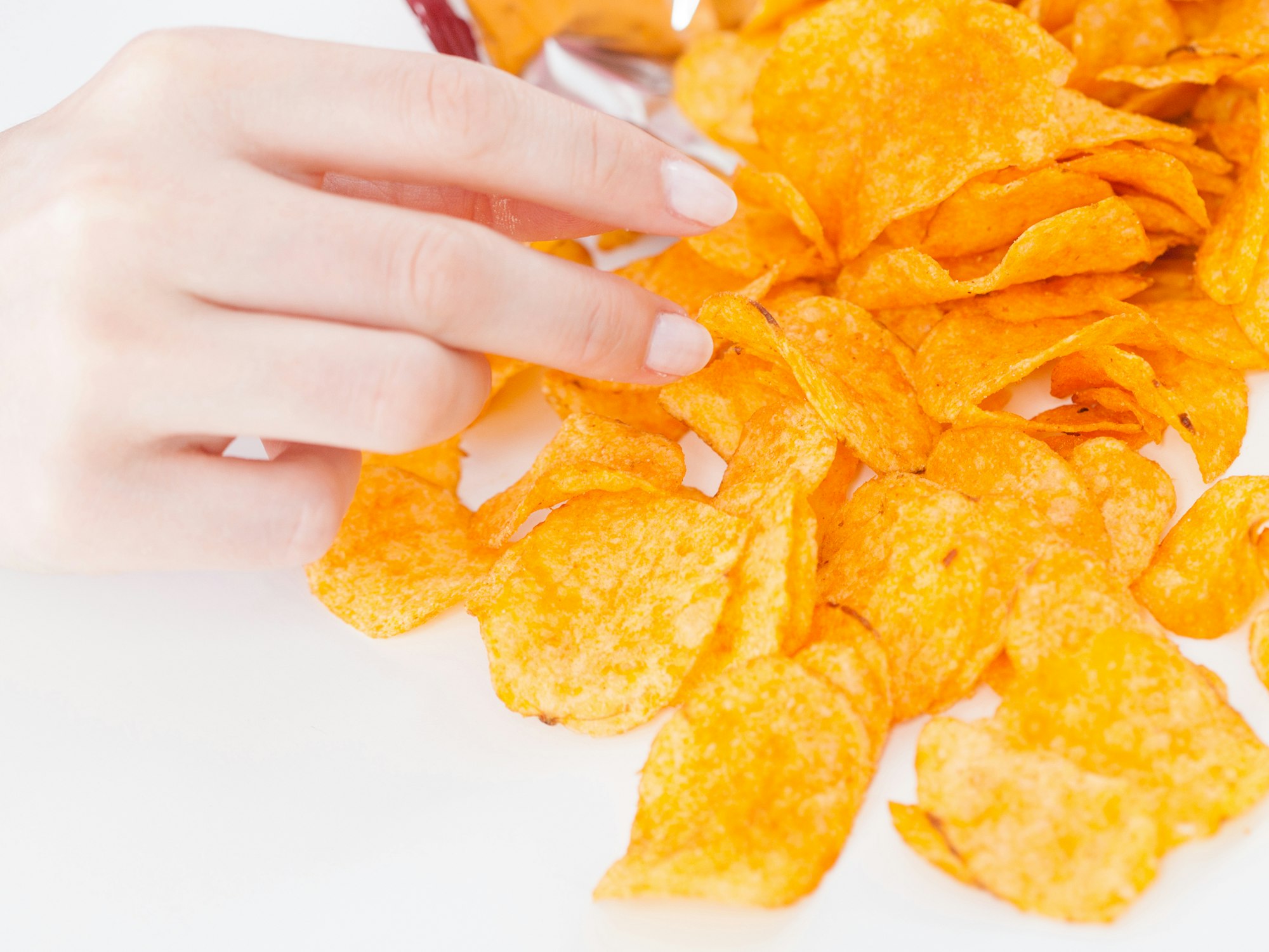 Das Symbolfoto zeigt eine Hand, die nach Kartoffelchips greift.