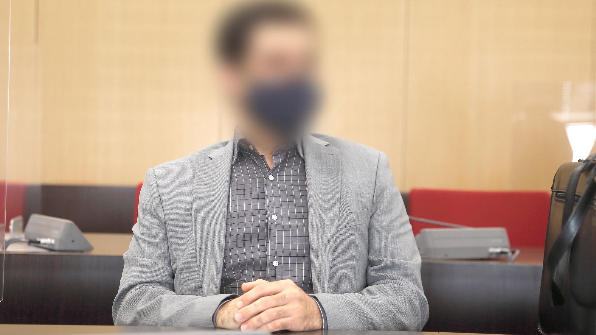 Der angeklagte Arzt sitzt mit Maske im Saal des Landgerichts
