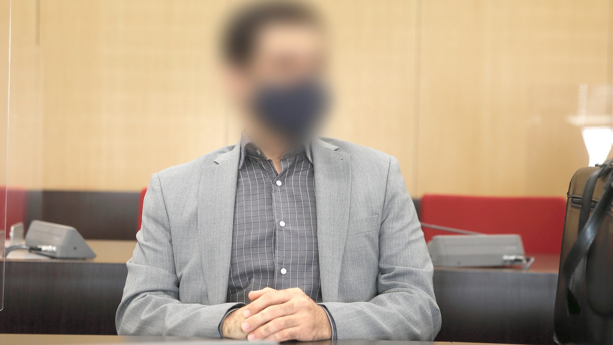 Der angeklagte Arzt sitzt mit Maske im Saal des Landgerichts