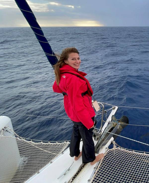 Mara Bergmann steht auf einem Katamaran, vor ihr schwimmen Delfine im Meer.