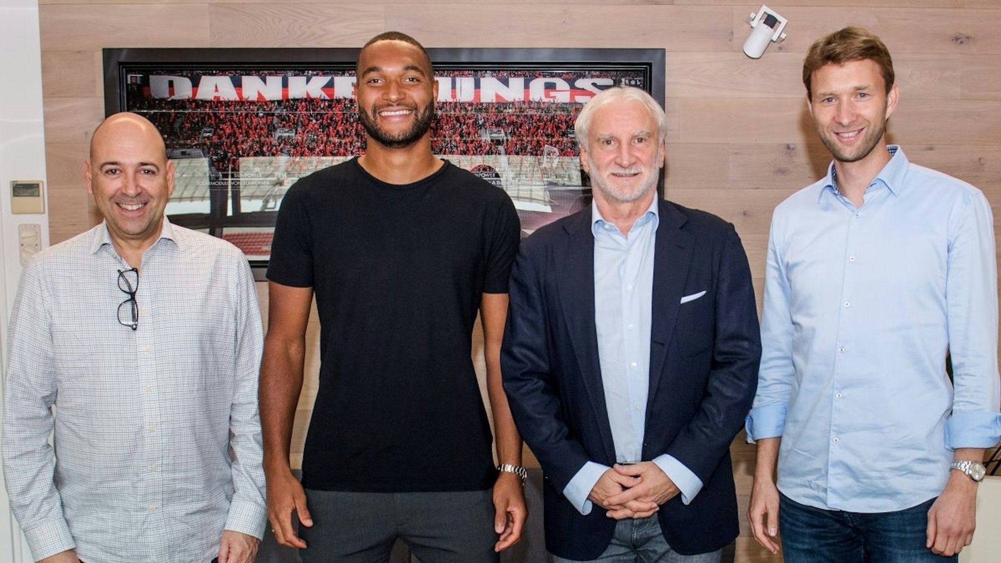 Jonathan Tah posiert zusammen mit Geschäftsführer Fernando Carro, Rudi Völler und Simon Rolfes vor einem Bild, das im Stadion aufgenommen worden ist.