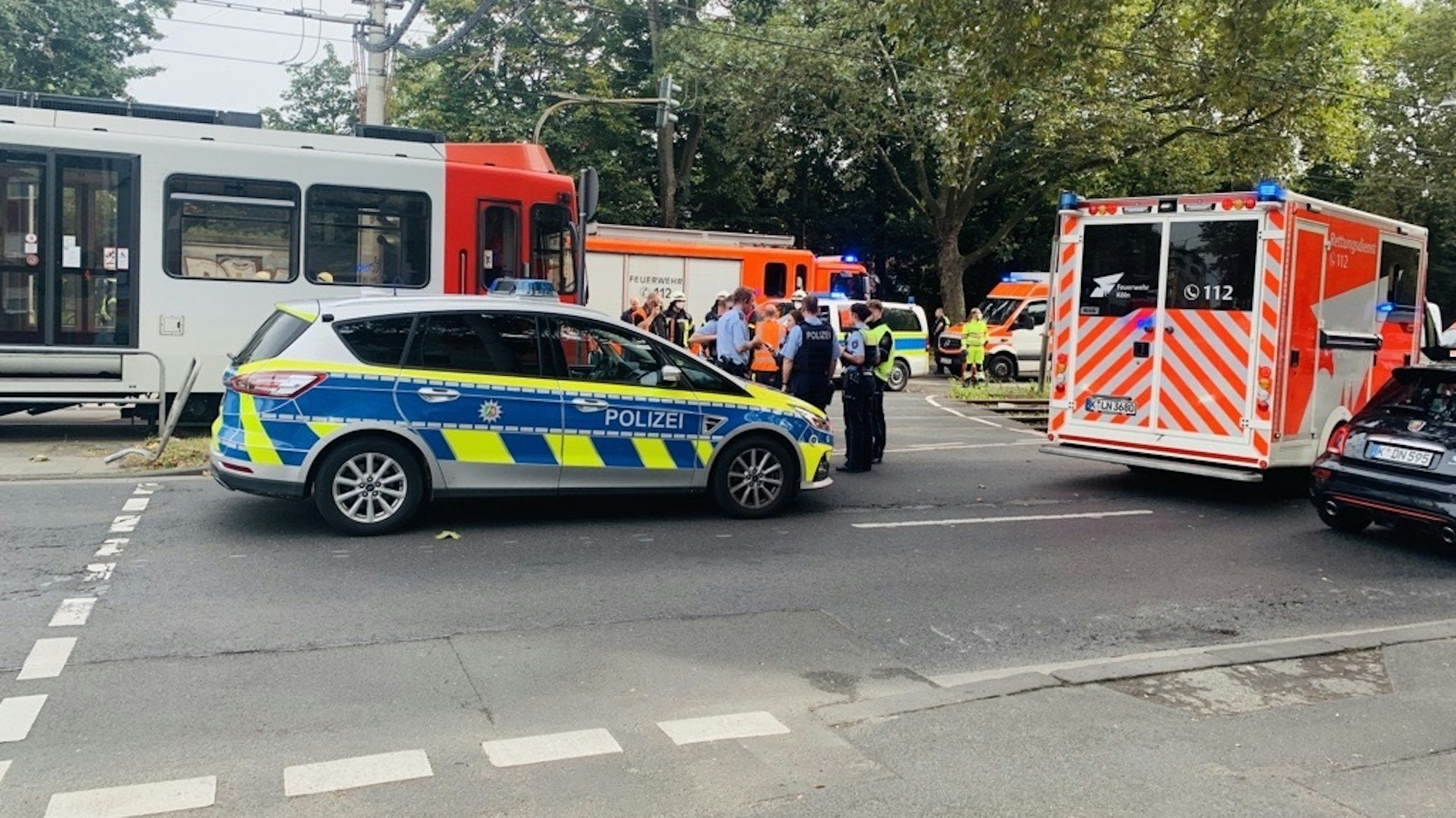 Einsatzfahrzeuge von Polizei, Feuerwehr und Rettungsdienst stehen auf der Straße, außerdem ein Pulk von Einsatzkräften. Eine Straßenbahn hat gestoppt.