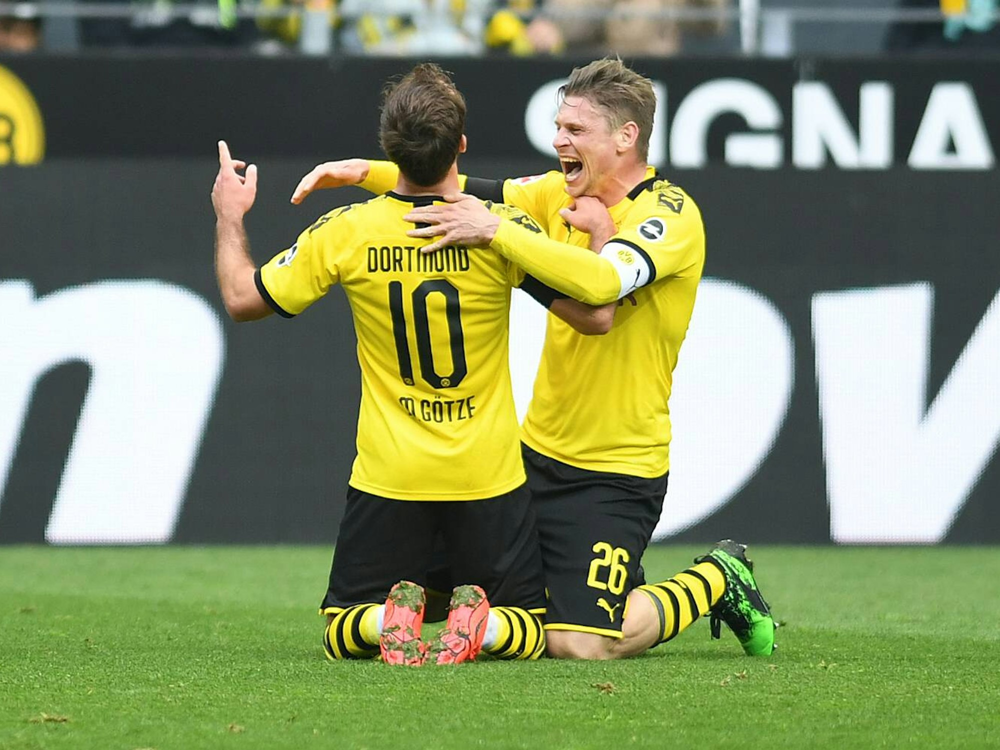 Mario Götze und Lukasz Piszczek knien auf dem Rasen, Piszczek will Götze umarmen.