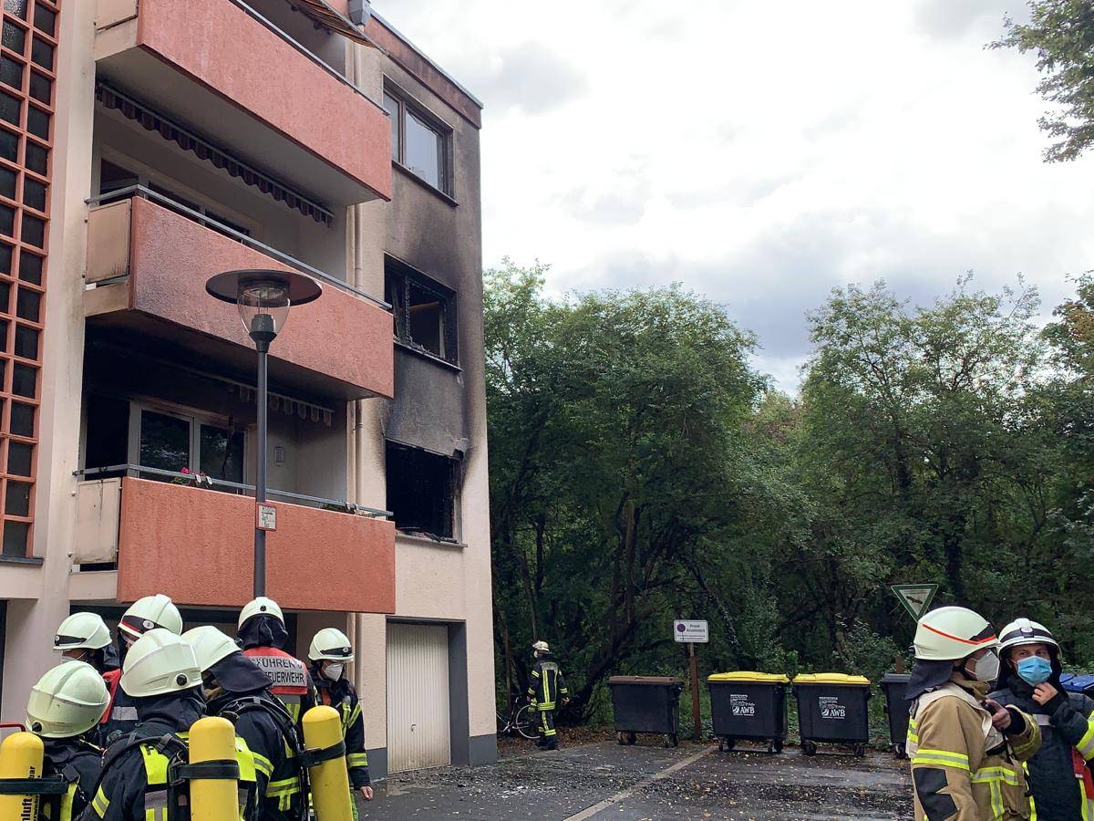 Feuerwehrmänner stehen vor dem Mehrfamilienhaus, in dem eine Küche in Flammen stand.