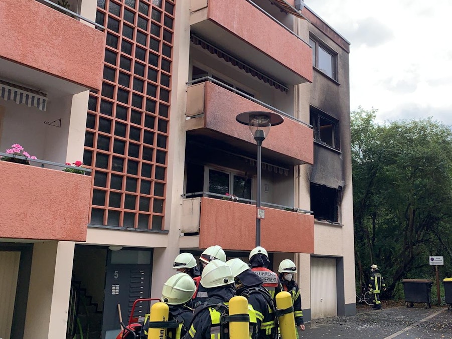 Feuerwehrmänner stehen vor dem Mehrfamilienhaus, in dem eine Küche in Flammen stand.