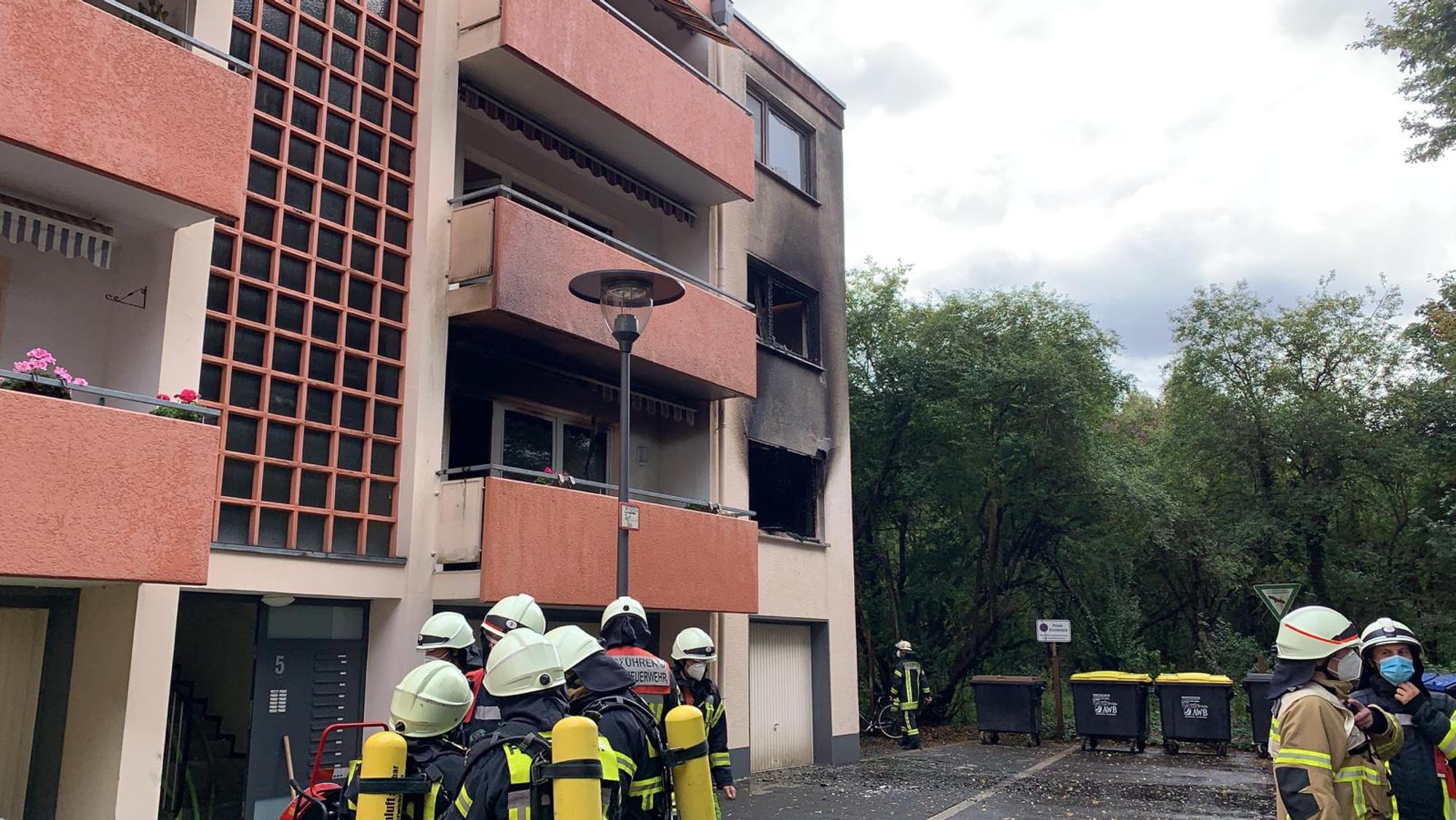 Feuerwehrmänner stehen vor dem Mehrfamilienhaus, in dem eine Küche in Flammen stand.