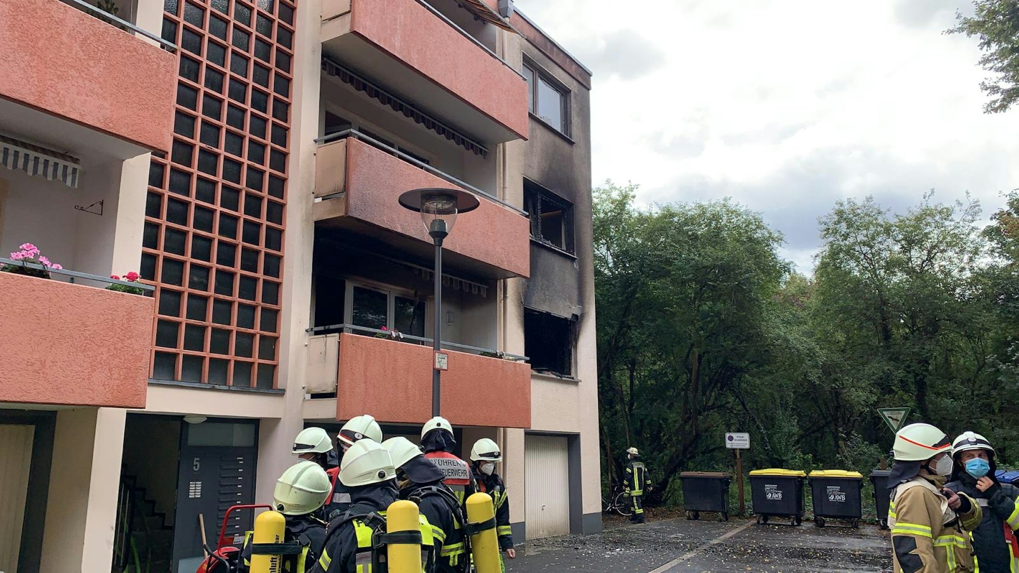 Feuerwehrmänner stehen vor dem Mehrfamilienhaus, in dem eine Küche in Flammen stand.