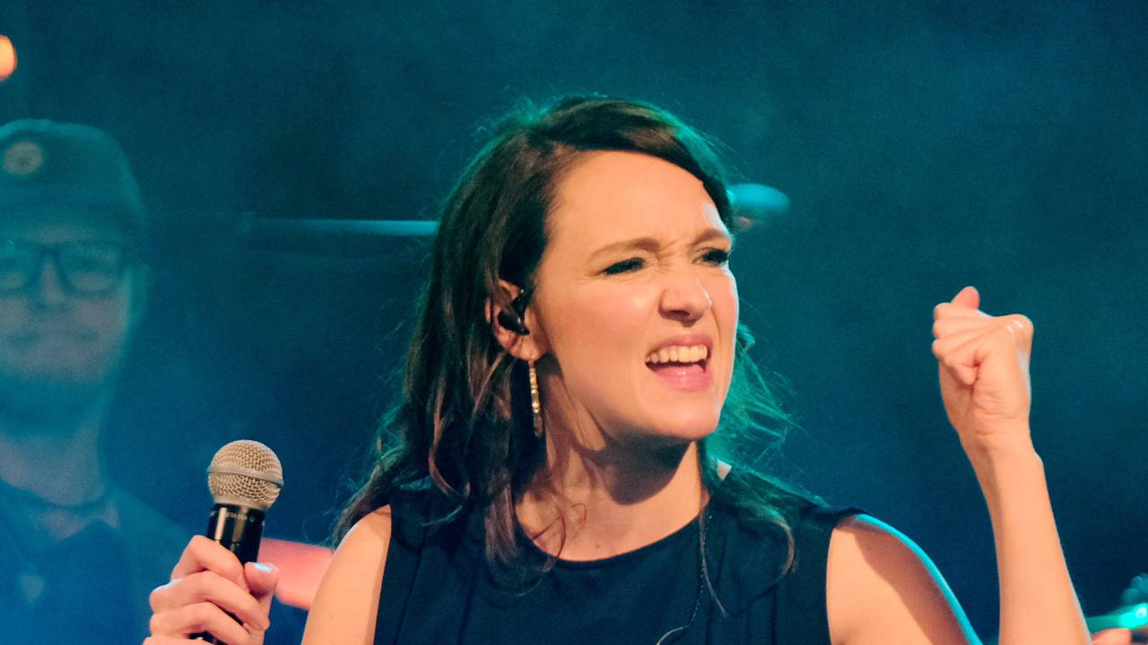 Carolina Kebekus steht mit einem Mikrofon in der Hand auf einer Bühne.