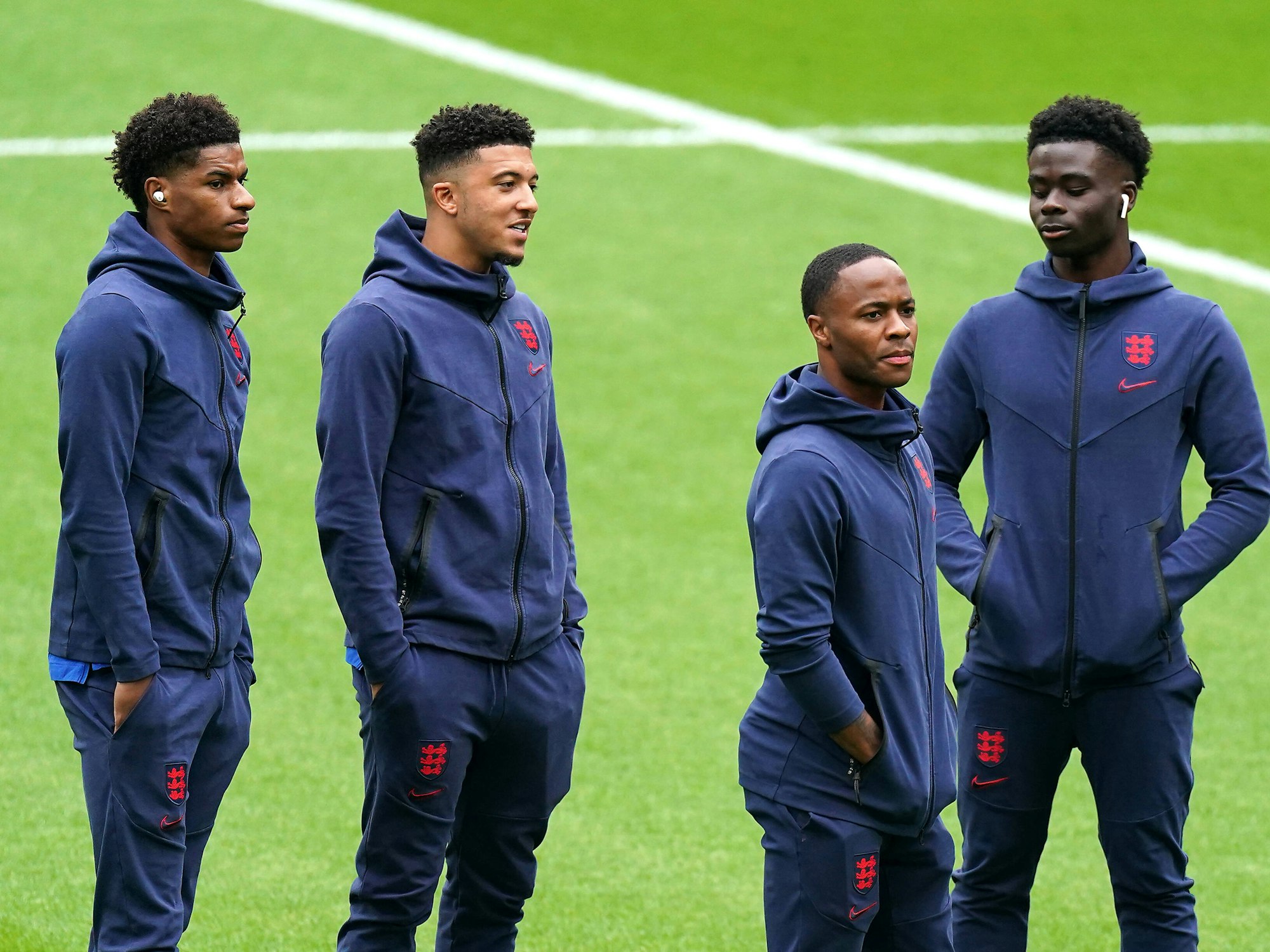 Marcus Rashford, Jadon Sancho und Bukayo Saka stehen zusammen mit Raheem Sterling auf dem Rasen. Sie tragen Trainingsanzüge englischen Nationalmannschaft.