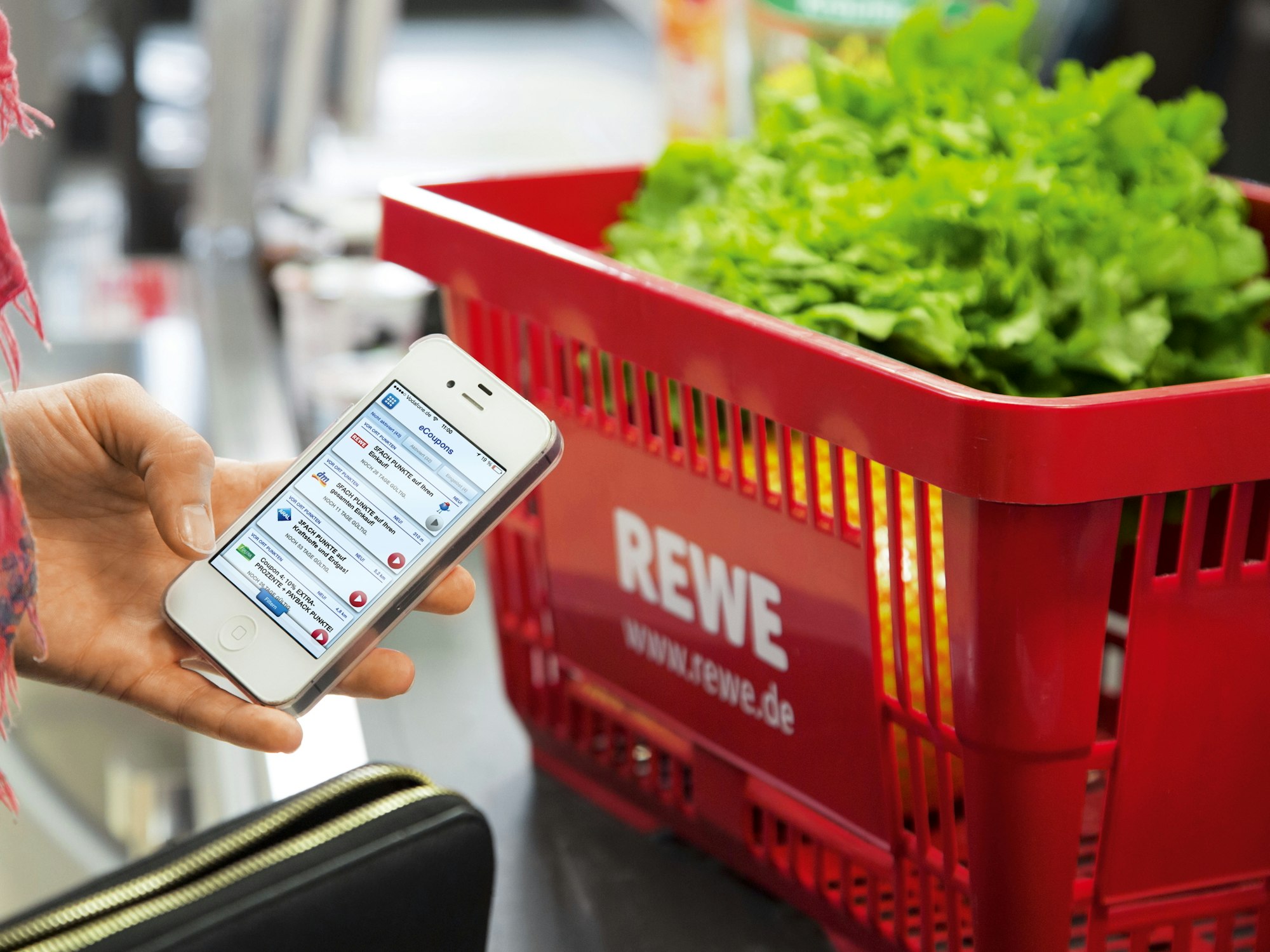 Das Symbolfoto zeigt eine Frau an der Kasse von Rewe. Sie hält ein Smartphone in der Hand mit einer Payback App.