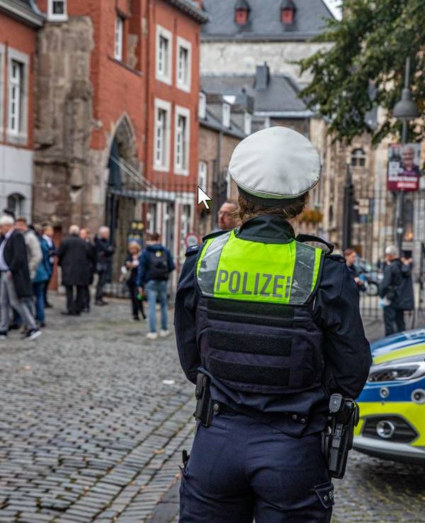 Zwei Polizisten stehen neben einem Einsatzwagen vor dem Aachener Dom.