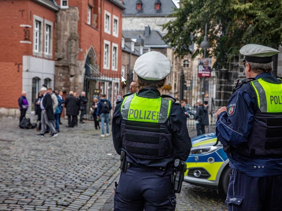 Zwei Polizisten stehen neben einem Einsatzwagen vor dem Aachener Dom.