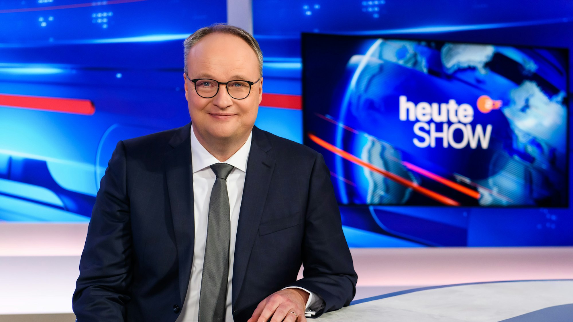 Oliver Welke steht im heute-show-Studio und lächelt in die Kamera.