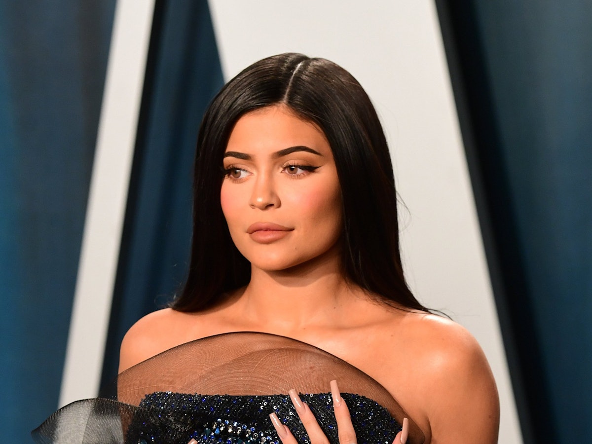 Kylie Jenner steht mit einem leichten Schmunzeln auf den Lippen vor einer blauen Wand. Die Hände hat sie auf ihre Brüste gelegt.