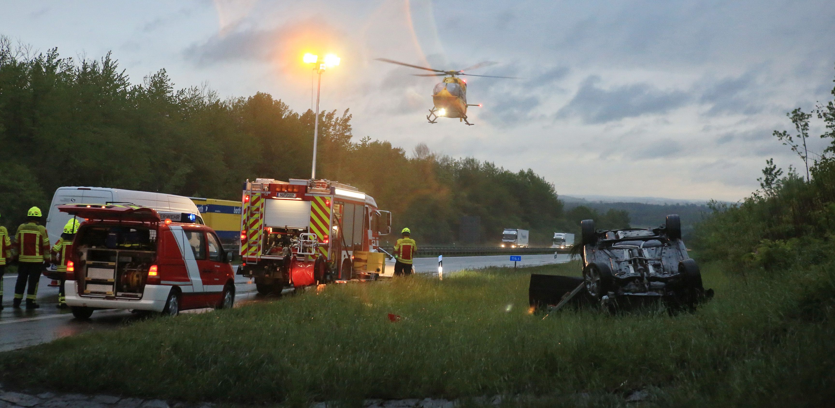Ein Auto liegt auf der A8 auf dem Grünstreifen. Ein Rettungshubschrauber ist im Anflug.