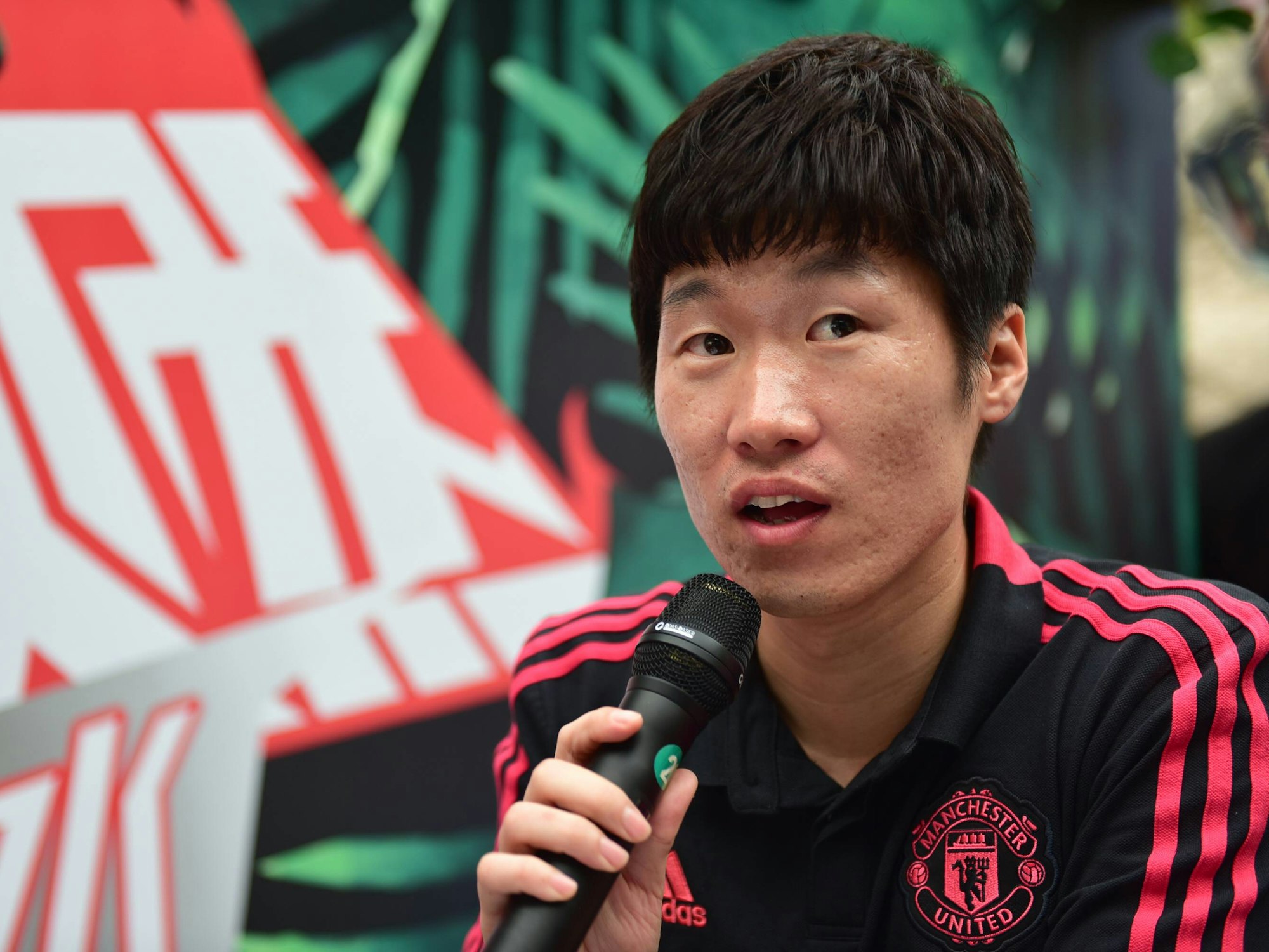 Ji-sung Park spricht in ein Mikrofon und trägt ein schwarz-rotes Shirt von Manchester-United.