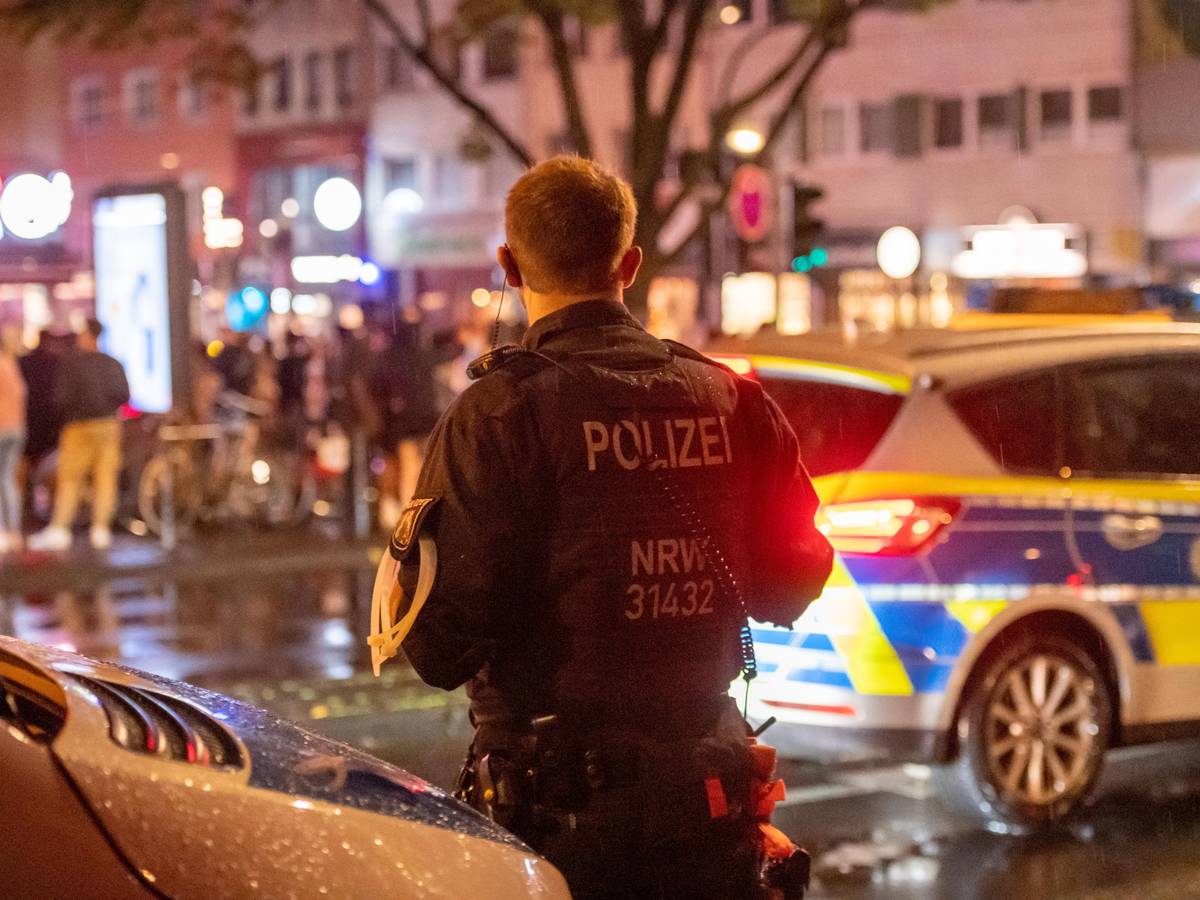 Ein Polizist einer Hundertschaft steht nachts neben einem Polizeiauto auf der Zülpicher Straße