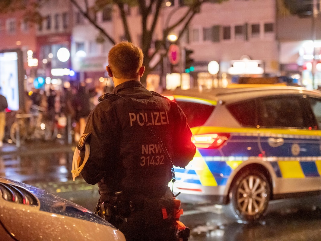 Ein Polizist einer Hundertschaft steht nachts neben einem Polizeiauto auf der Zülpicher Straße