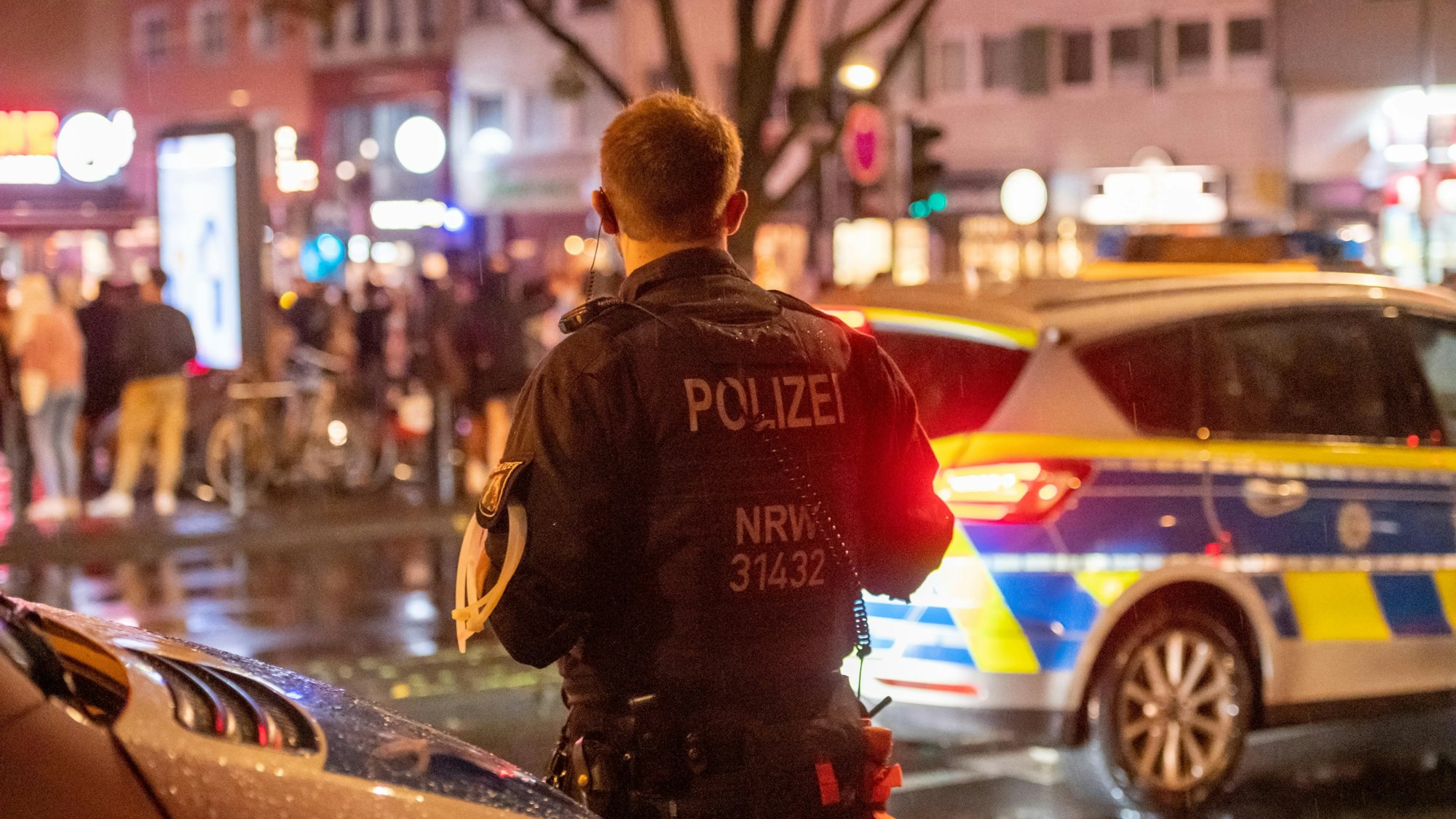 Ein Polizist einer Hundertschaft steht nachts neben einem Polizeiauto auf der Zülpicher Straße