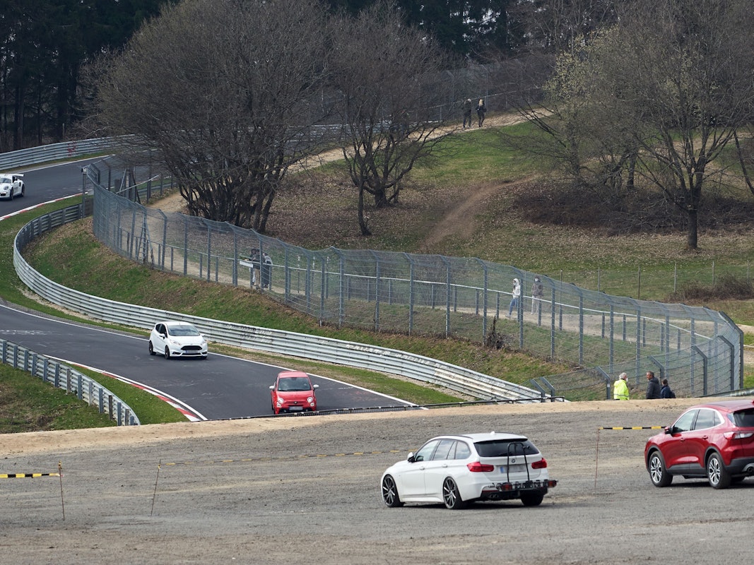 Das Symbolbild zeigt die Nordschleife des Nürburgrings im April 2021, mehrere Autos fahren auf der Strecke, einige Menschen stehen am Rand und schauen zu.