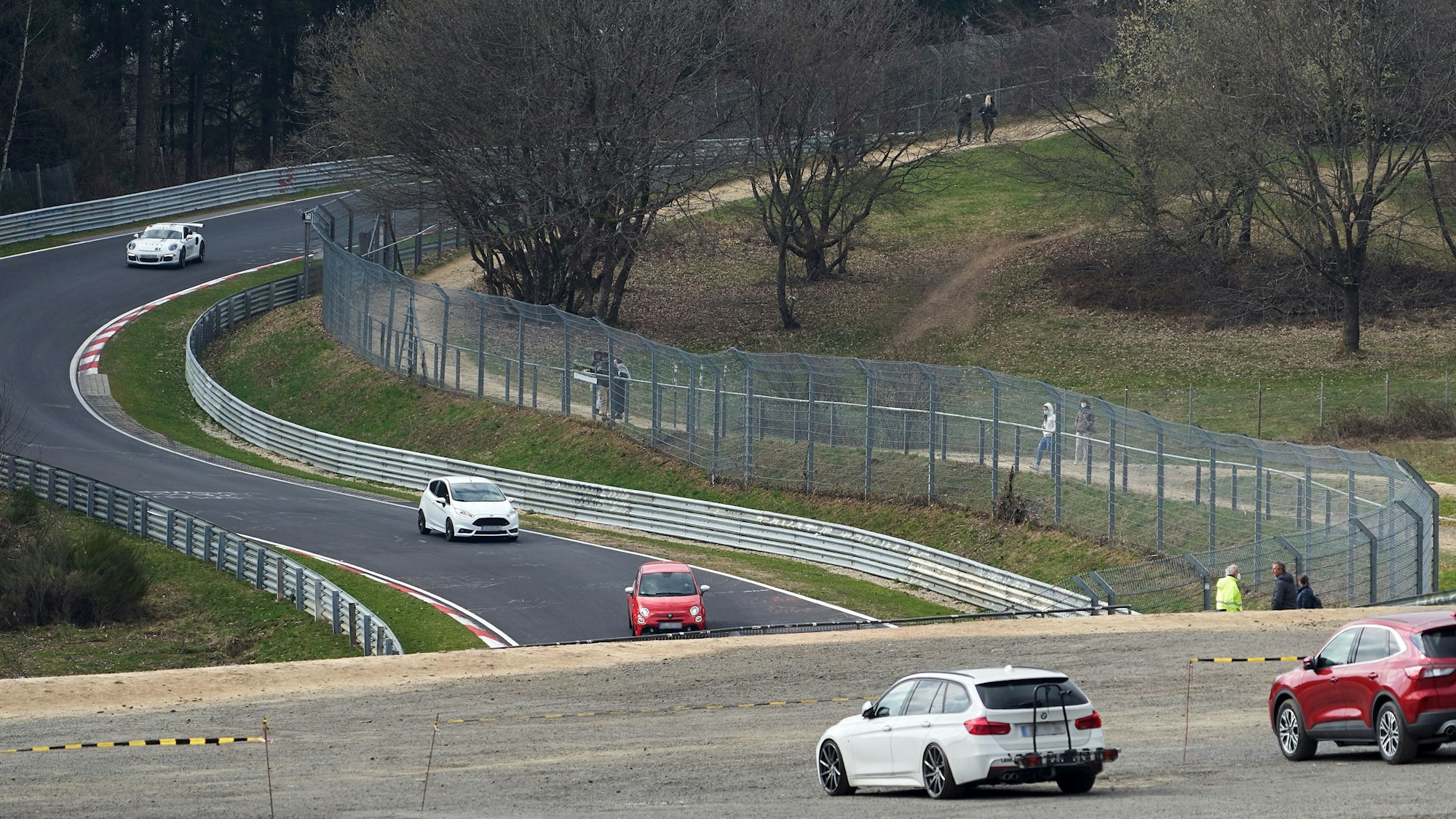 Das Symbolbild zeigt die Nordschleife des Nürburgrings im April 2021, mehrere Autos fahren auf der Strecke, einige Menschen stehen am Rand und schauen zu.