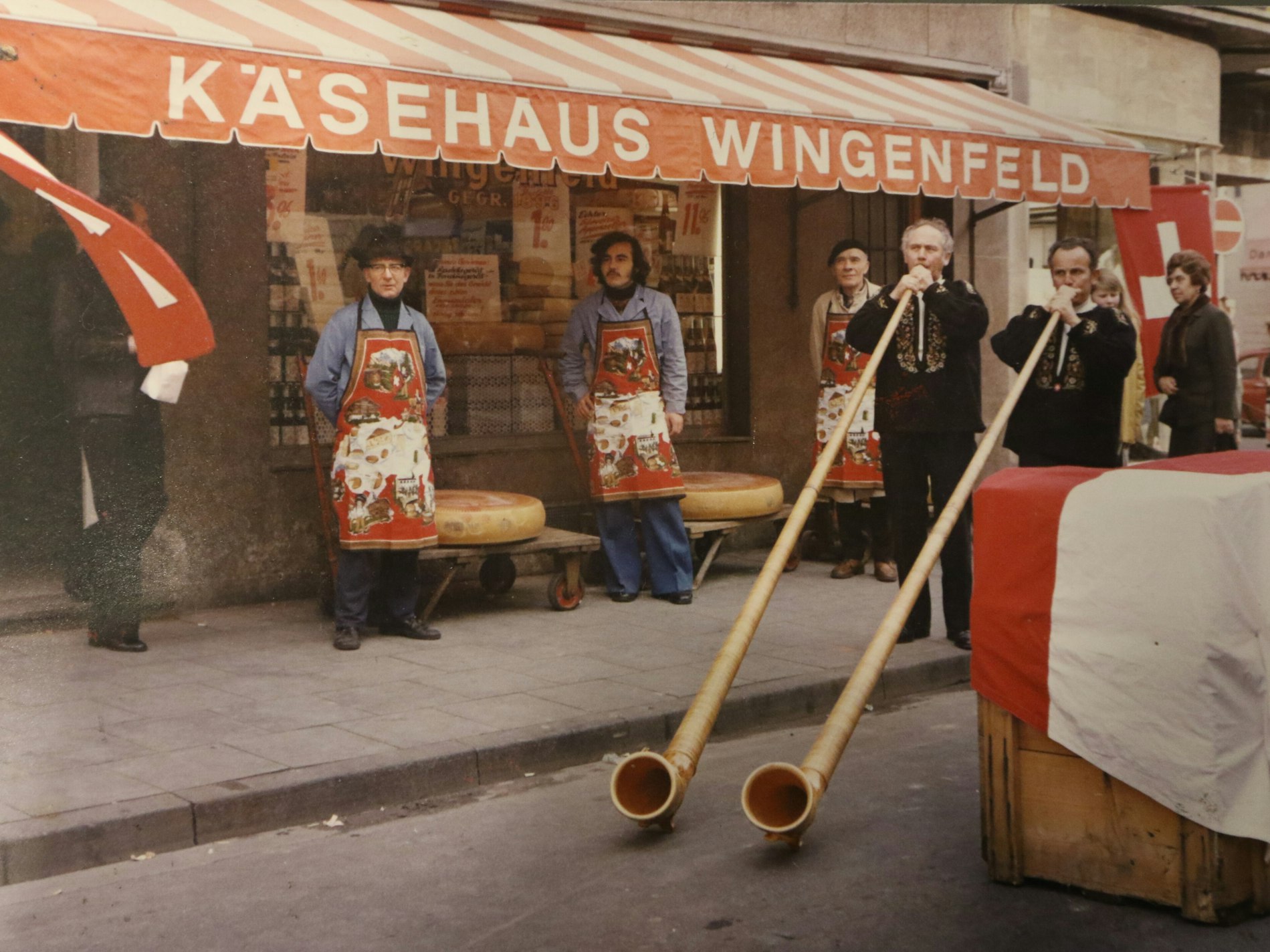 Mitarbeiter stehen mit Alphörnern vor einem Käsegeschäft.
