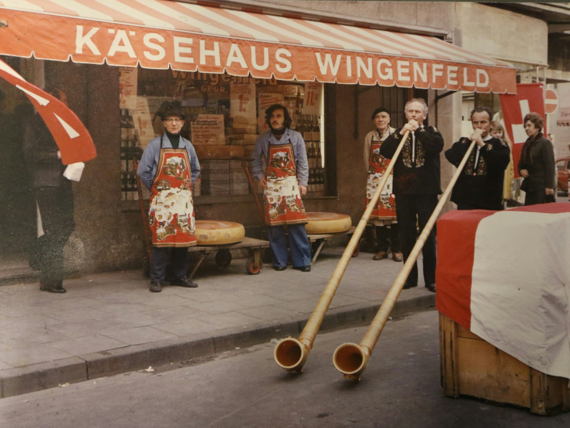 Mitarbeiter stehen mit Alphörnern vor einem Käsegeschäft.