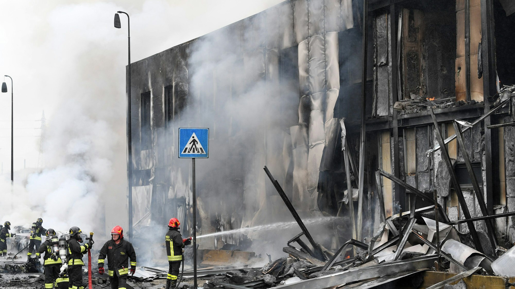 Ein Kleinflugzeug stürzt in Mailand am Sonntag (3. Oktober) nur Augenblicke nach dem Start ab und in ein Bürogebäude. Feuerwehrleute löschen die Trümmer des Gebäudes, Qualm steigt auf.