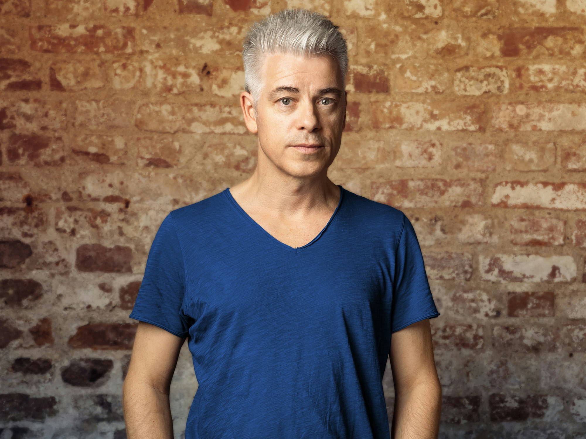 Comedian Michael Mittermeier steht mit ernstem Blick vor einer Steinwand und schaut in die Kamera.