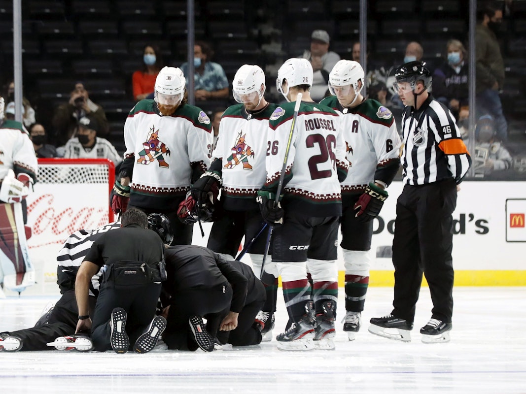 Die Spieler der Arizona Coyotes versammeln sich bei einem NHL-Vorbereitungsspiel um den am Boden liegenden Schiedsrichter Ryan Gibbons, der von Medizinern behandelt wird.