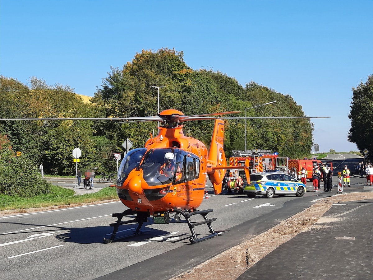 Ein Rettungshubschrauber ist auf einer Fahrbahn gelandet. Im Hintergrund stehen Einsatzfahrzeuge von Polizei und Feuerwehr.