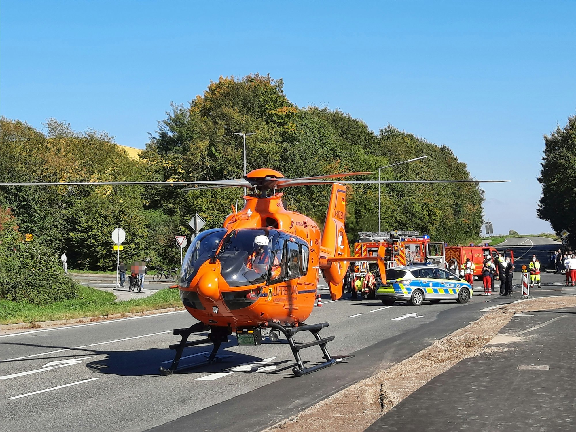 Ein Rettungshubschrauber ist auf einer Fahrbahn gelandet. Im Hintergrund stehen Einsatzfahrzeuge von Polizei und Feuerwehr.