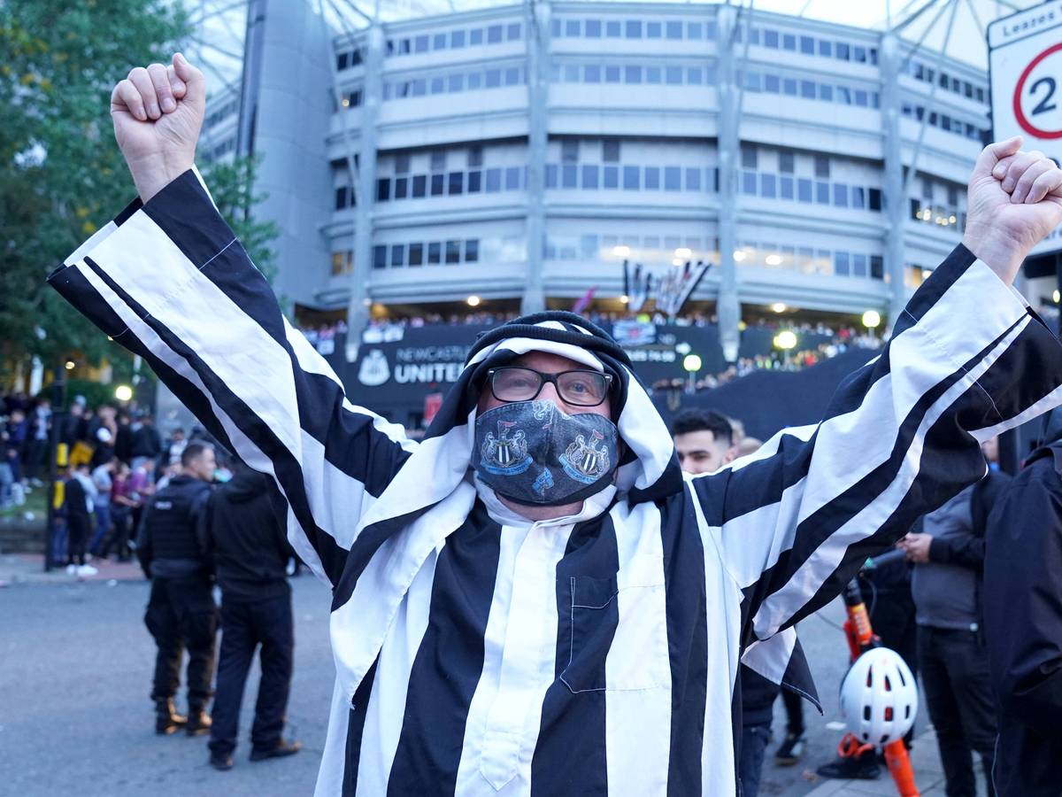 Ein Fan von Newcastle trägt eine arabische Kopfbedeckung und streckt die Arme zum Jubeln in die Höhe.