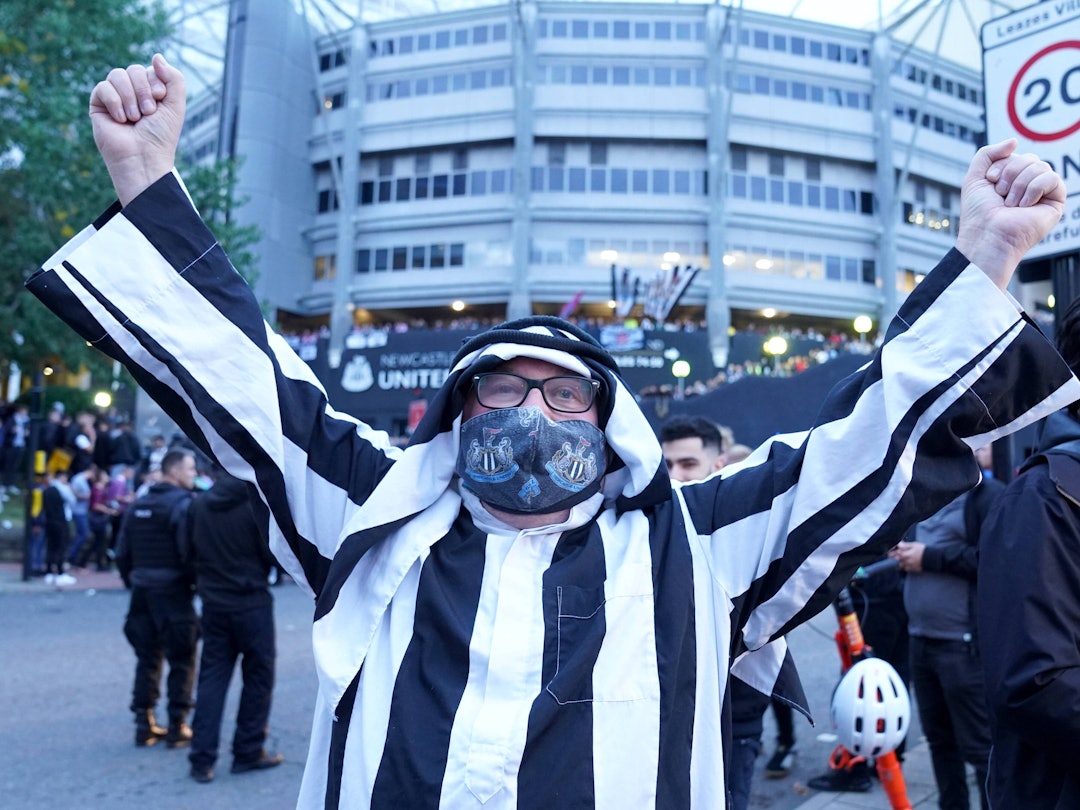 Ein Fan von Newcastle trägt eine arabische Kopfbedeckung und streckt die Arme zum Jubeln in die Höhe.