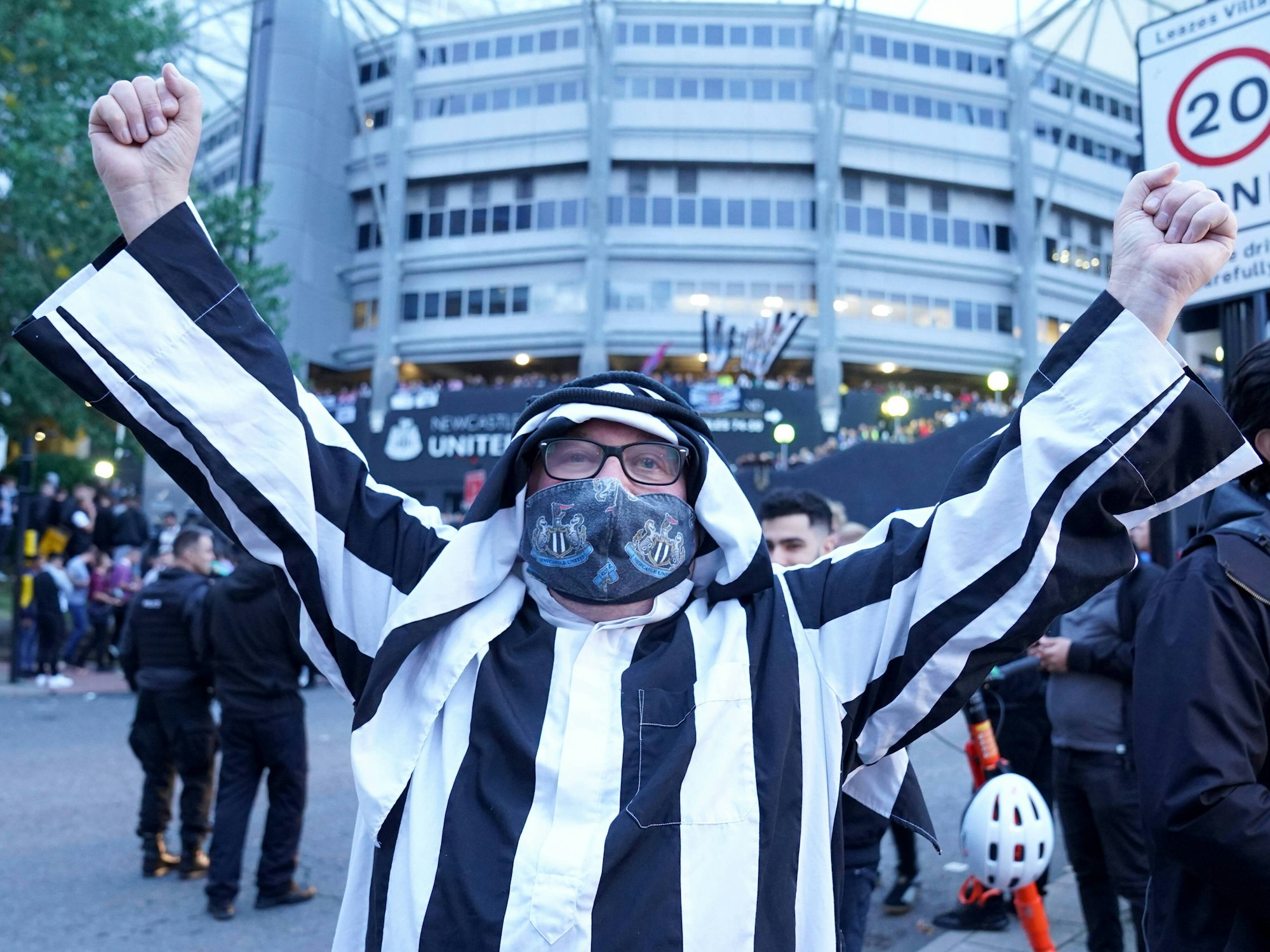 Ein Fan von Newcastle trägt eine arabische Kopfbedeckung und streckt die Arme zum Jubeln in die Höhe.