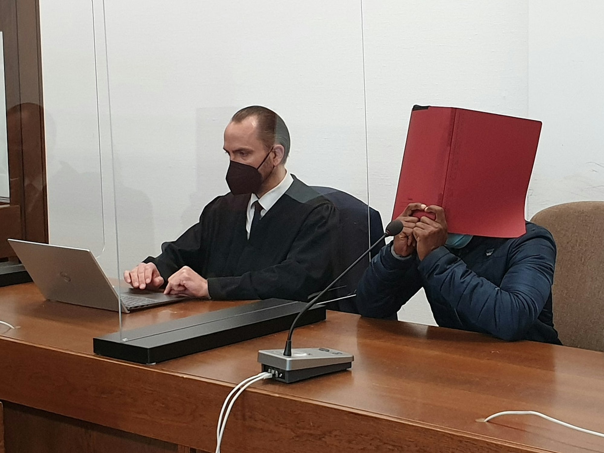 Angeklagter Richard L hält sich eine rote Akte vors Gesicht.