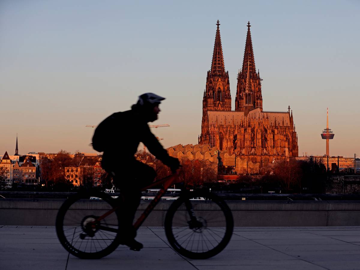 Ein Radfahrer fährt am Morgen am Dom vorbei, der von der aufgehenden Sonne angeleuchtet wird.