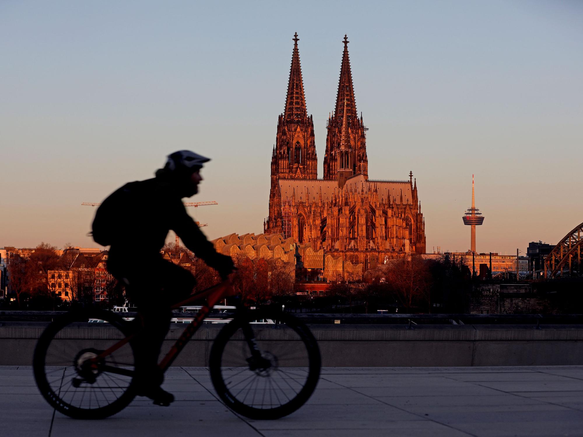 Ein Radfahrer fährt am Morgen am Dom vorbei, der von der aufgehenden Sonne angeleuchtet wird.