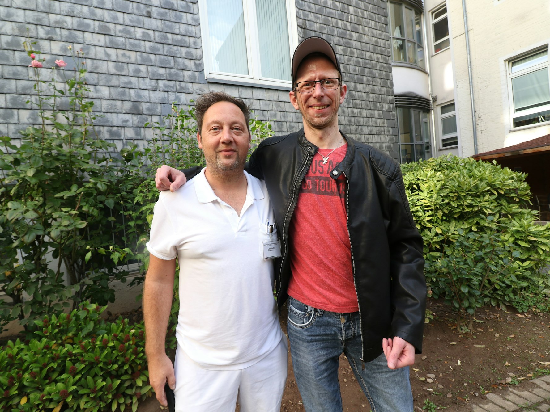Daniel Fuchs und Jörg Müller stehen zusammen im Hof eines Krankenhauses.