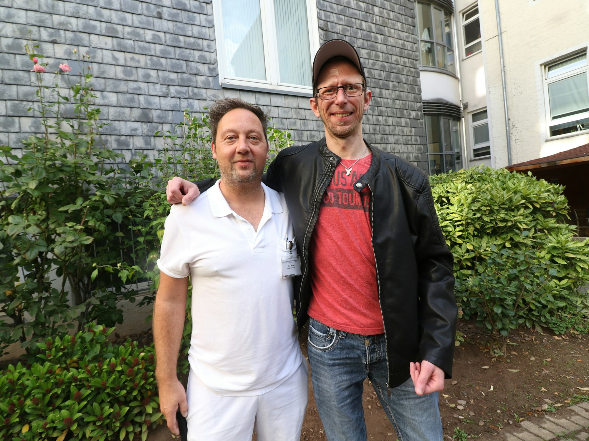 Daniel Fuchs und Jörg Müller stehen zusammen im Hof eines Krankenhauses.