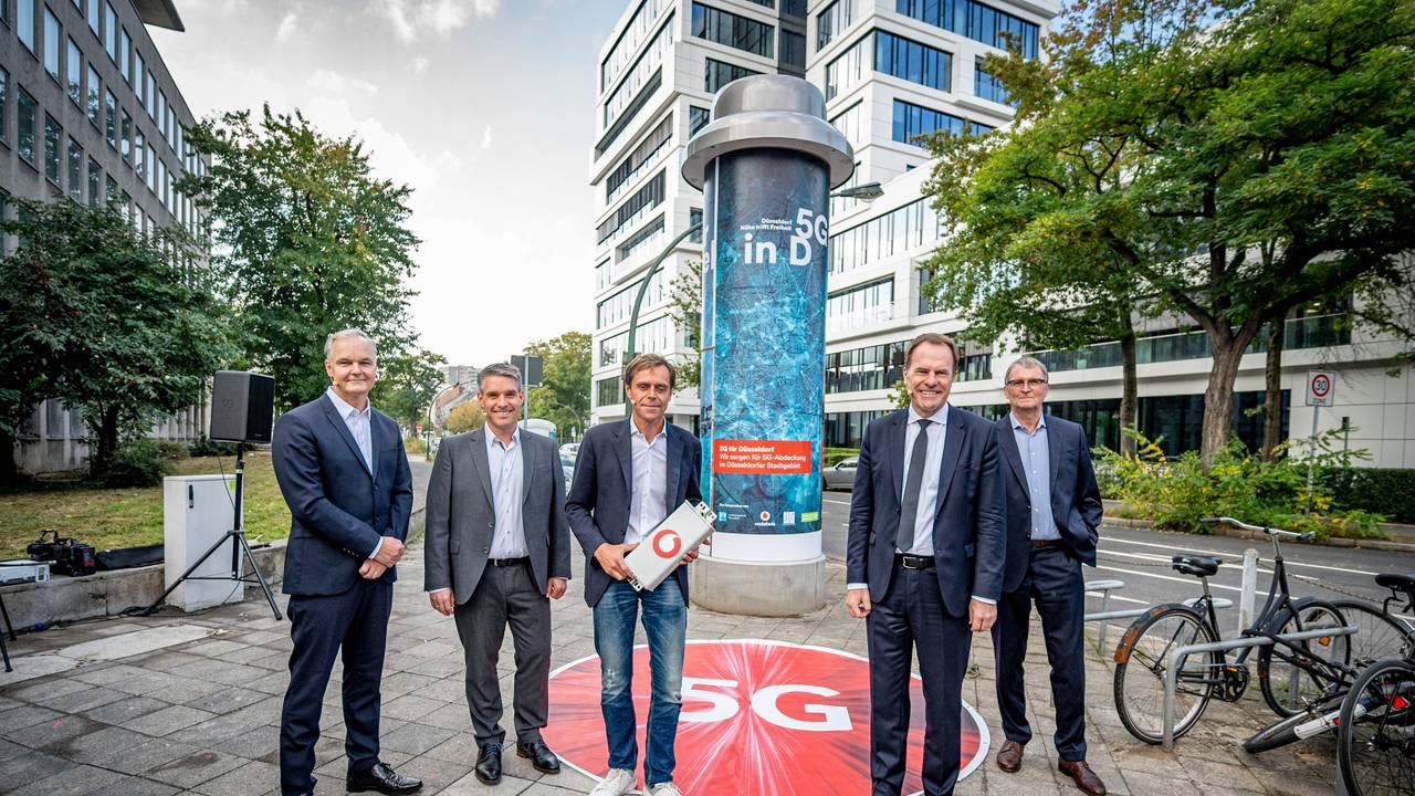 Alle Beteiligten stehen vor einer Litfaßsäule in Düsseldorf.
